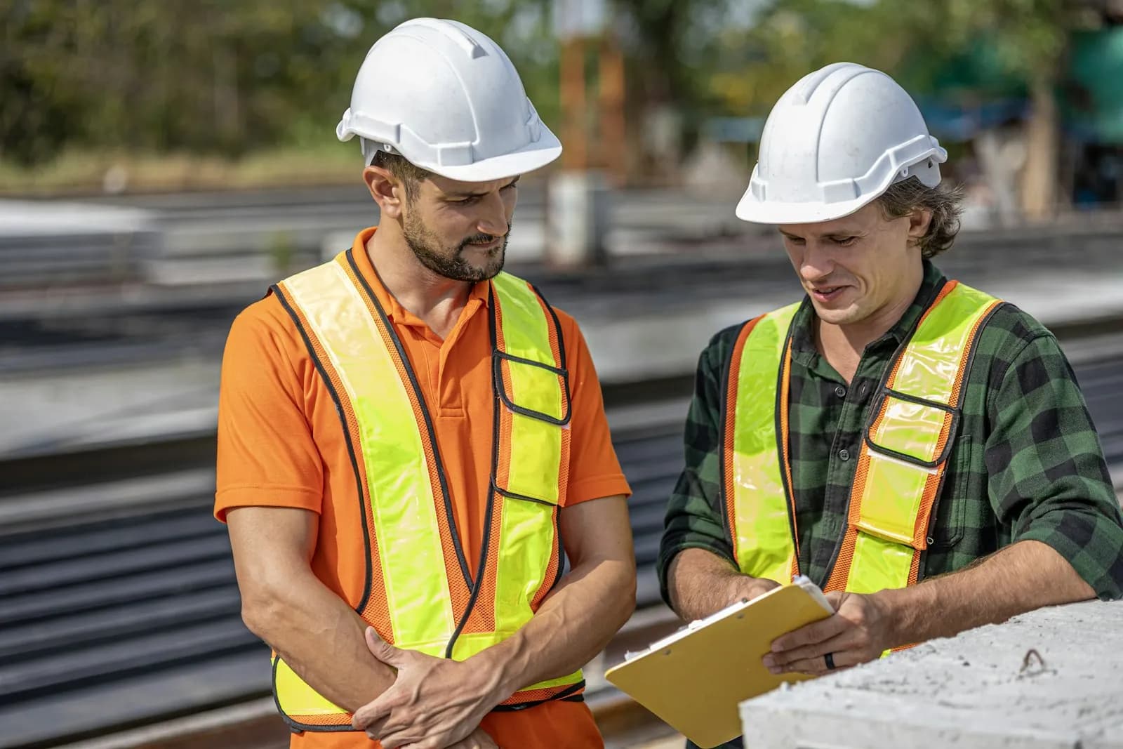 Two construction workers in safety vests reviewing a clipboard on site