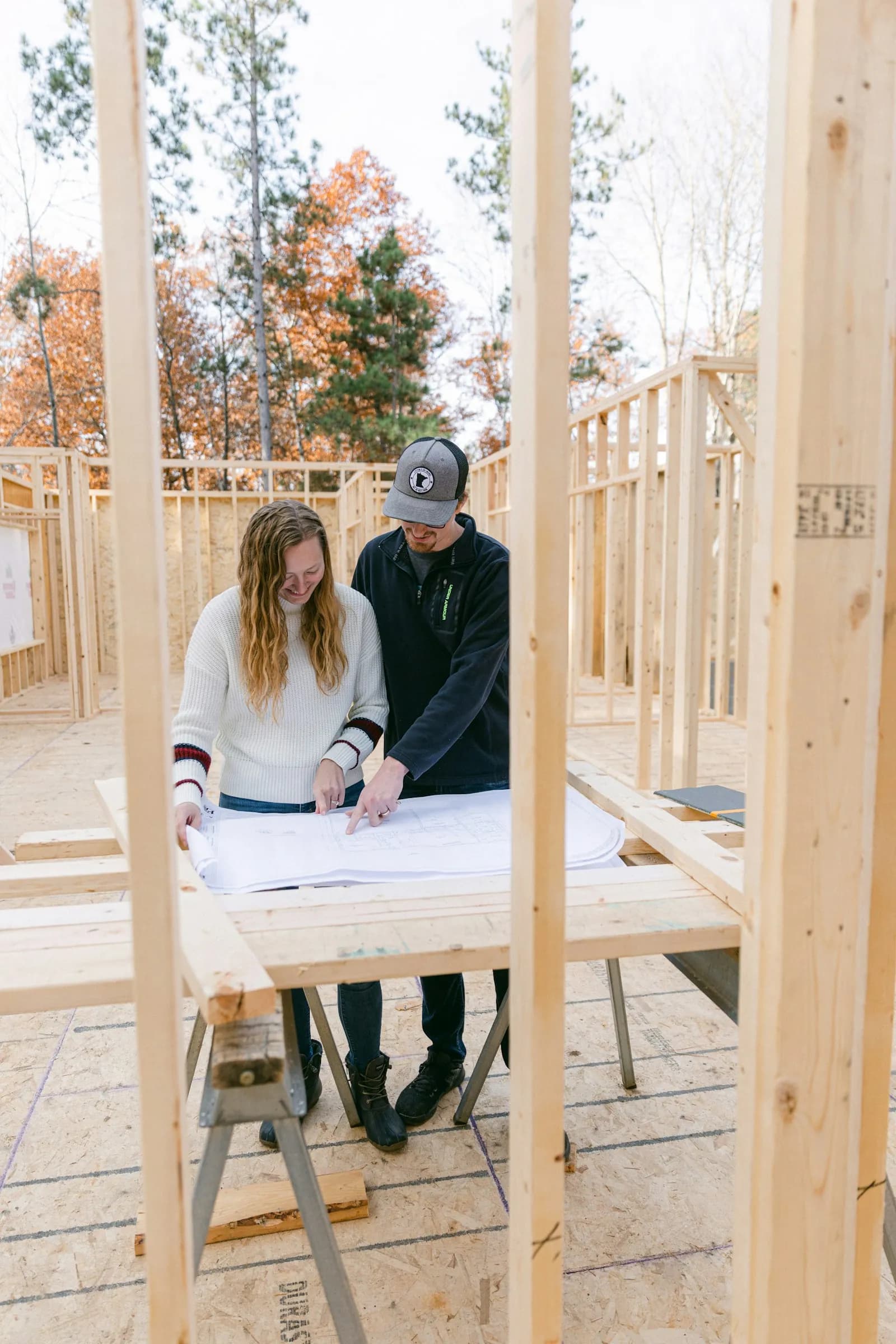 Two people reviewing building plans inside a wood-framed house